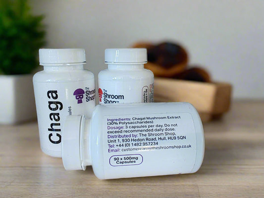 Three white supplement bottles labeled 'Chaga', 'The Shroom Shop', and 'Polyporus' on a wooden surface with a tiled wall background.
